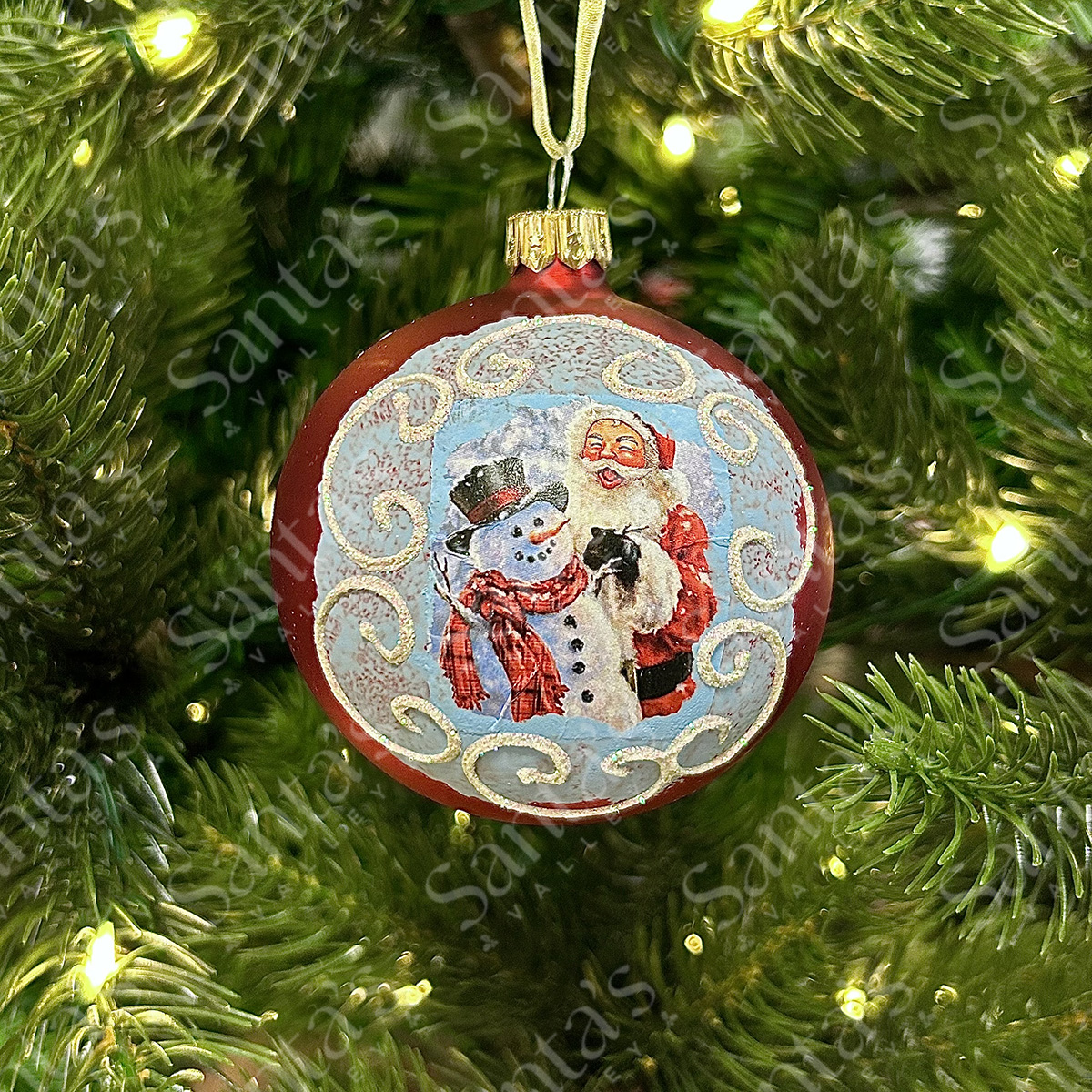 Boule de Noël rouge avec le Père Noël et un bonhomme de neige sur un fond bleu.