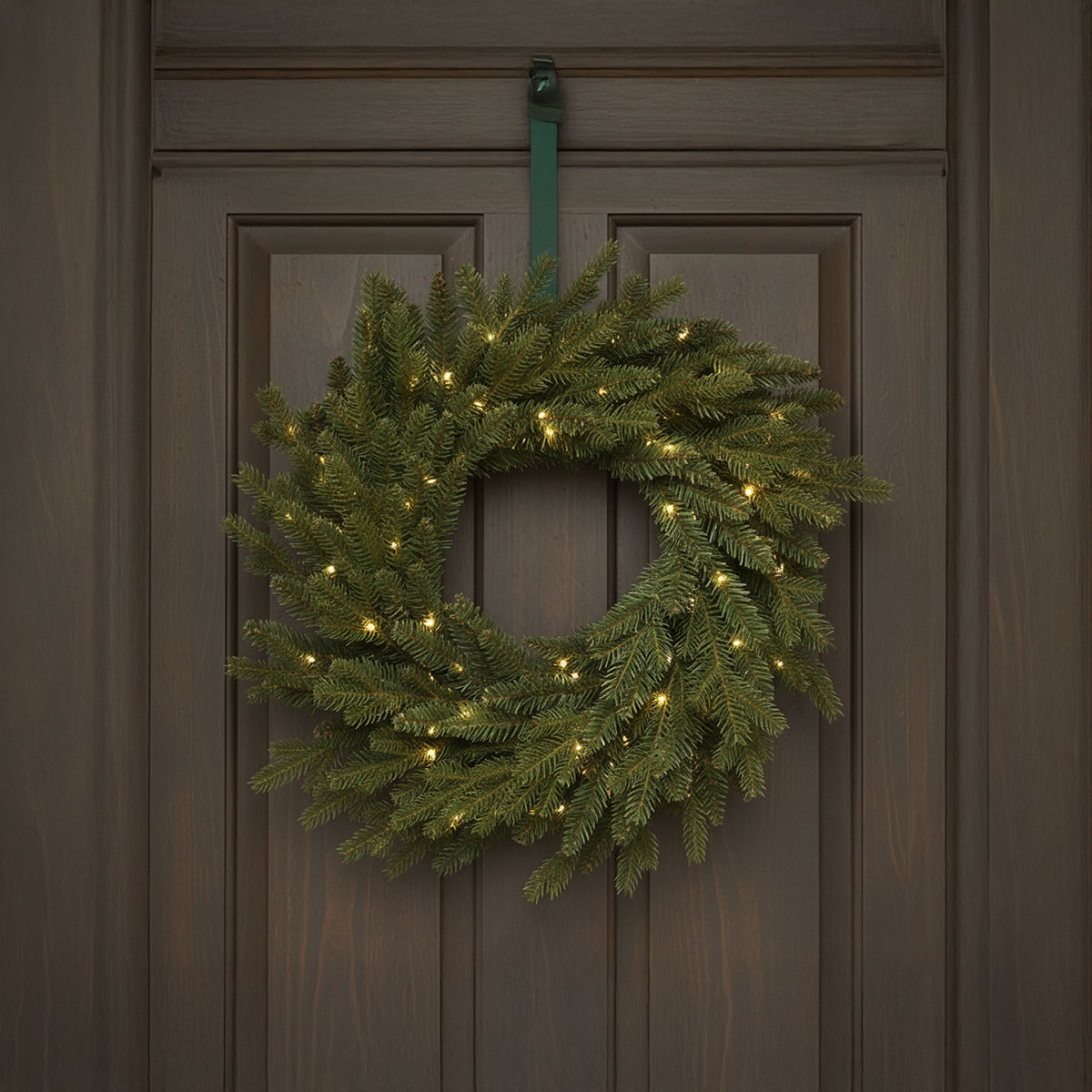 Corona di abete illuminata appesa a una porta di legno scuro
