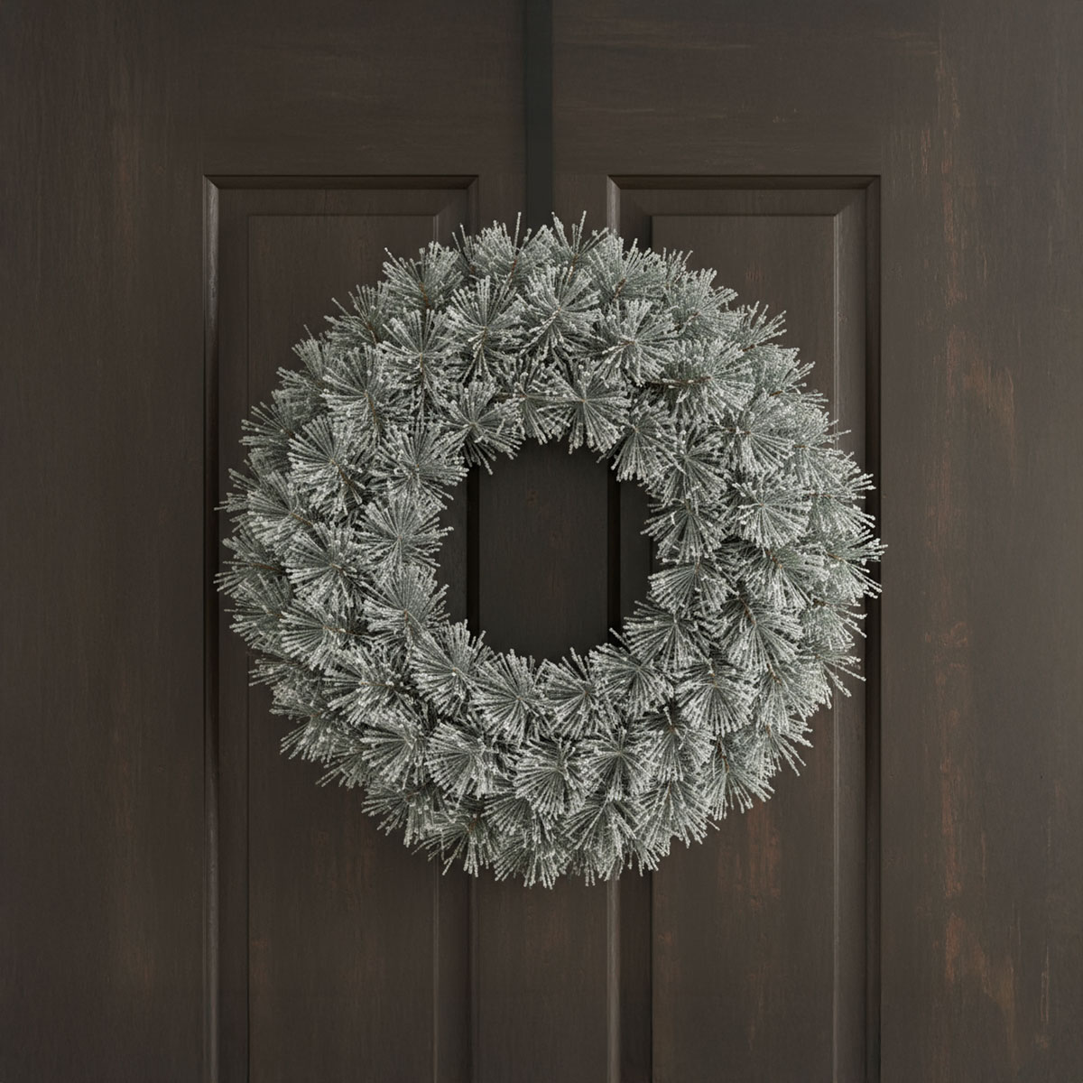 Couronne de sapin givrée suspendue à une porte en bois sombre