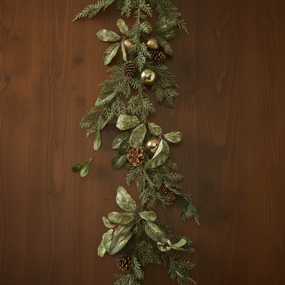 Guirlande de Noël avec des feuilles vertes, des pommes de pin et des boules dorées sur fond de bois