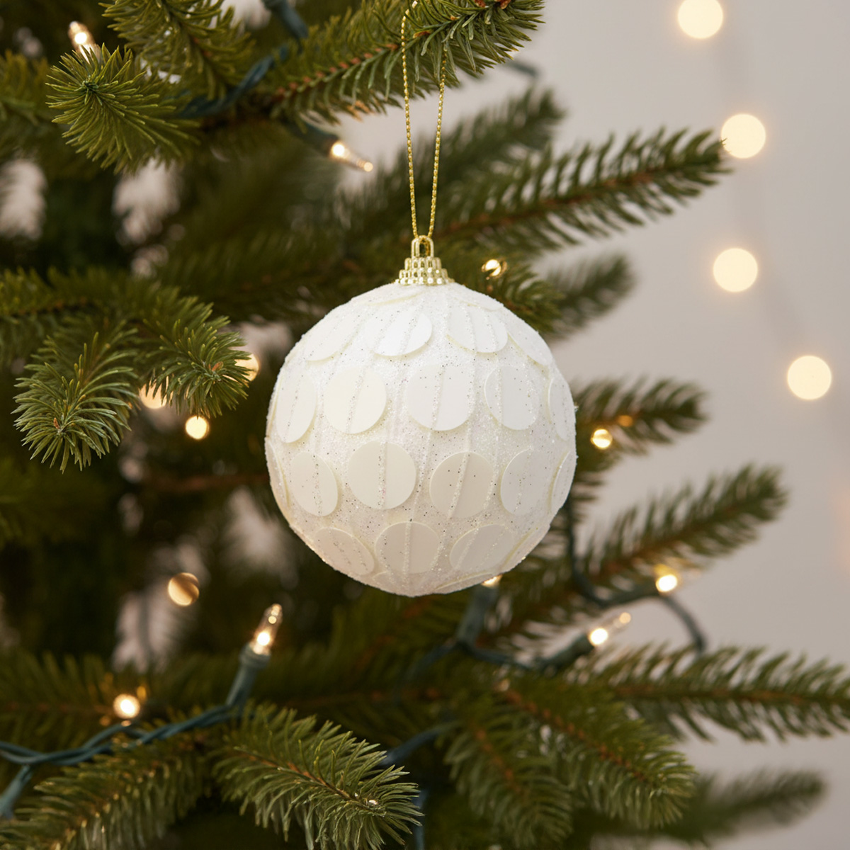 Boule de Noël blanche texturée sur un sapin décoré de lumières