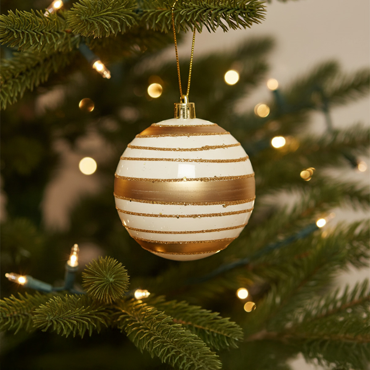 Adorno navideño blanco con rayas doradas en un árbol decorado