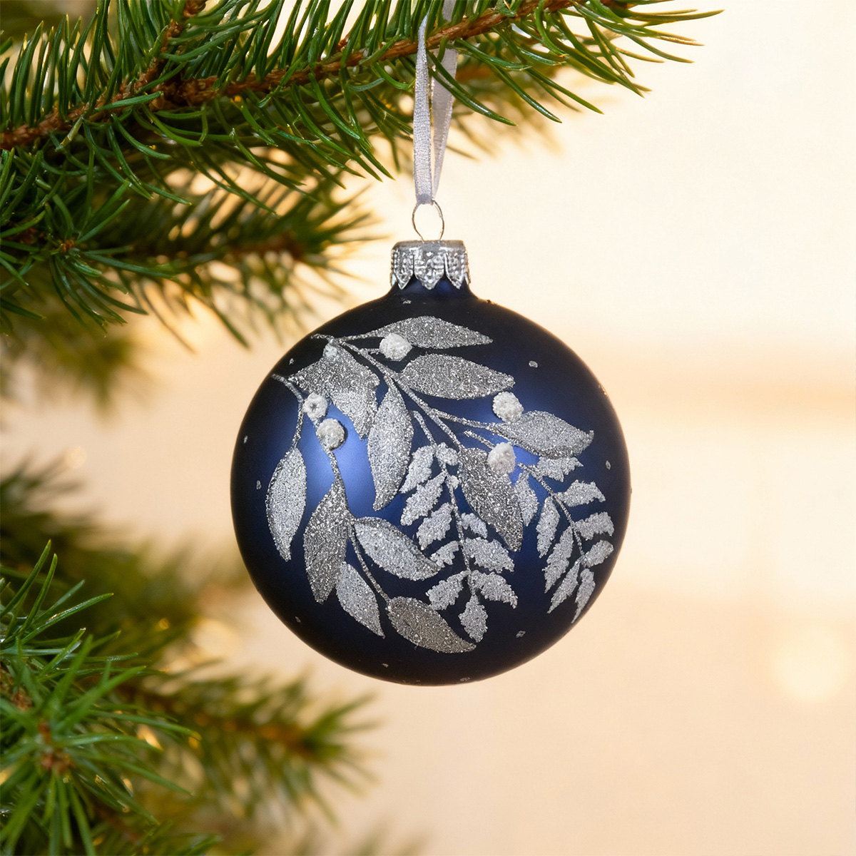 Boule de Noël bleue ornée de feuilles argentées sur une branche de sapin