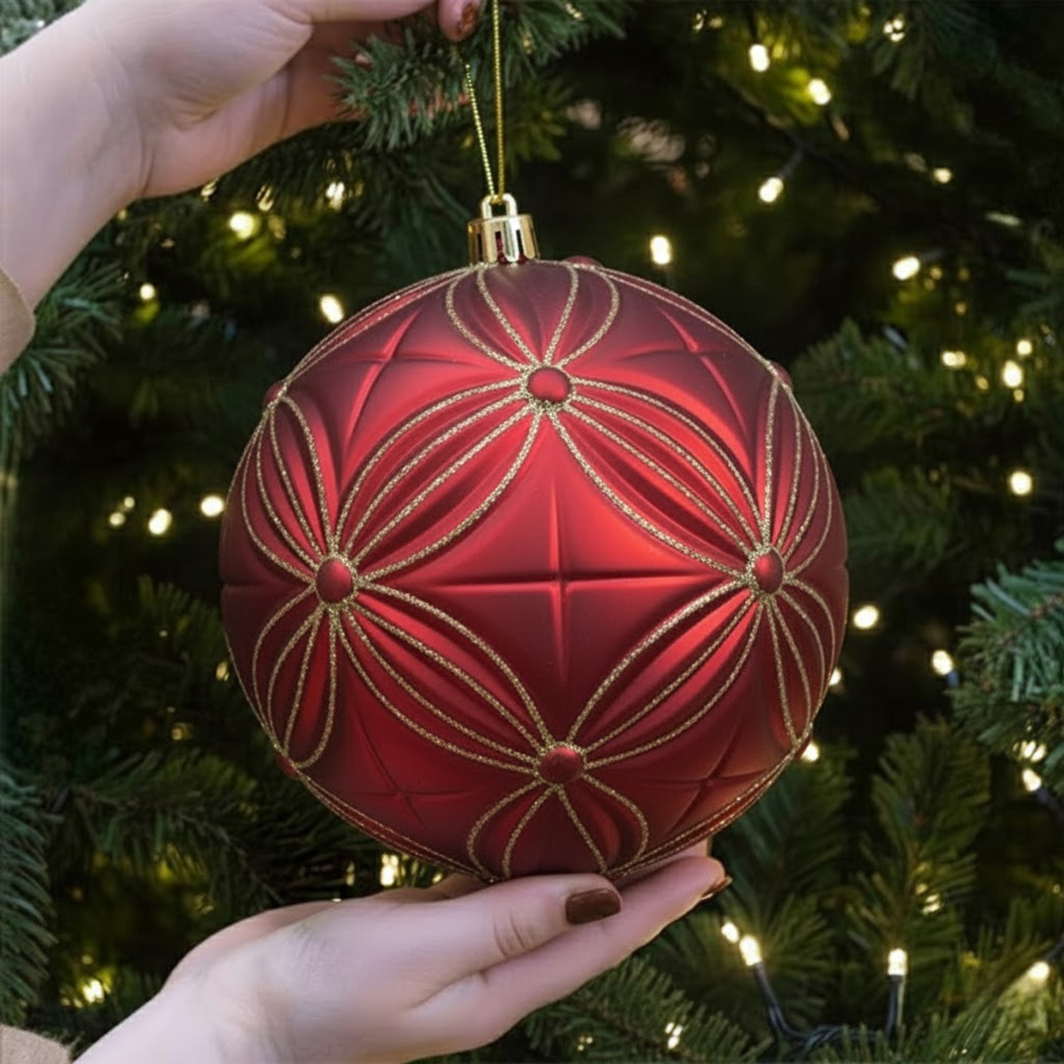 Boule de Noël rouge ornée de motifs dorés, tenue par des mains