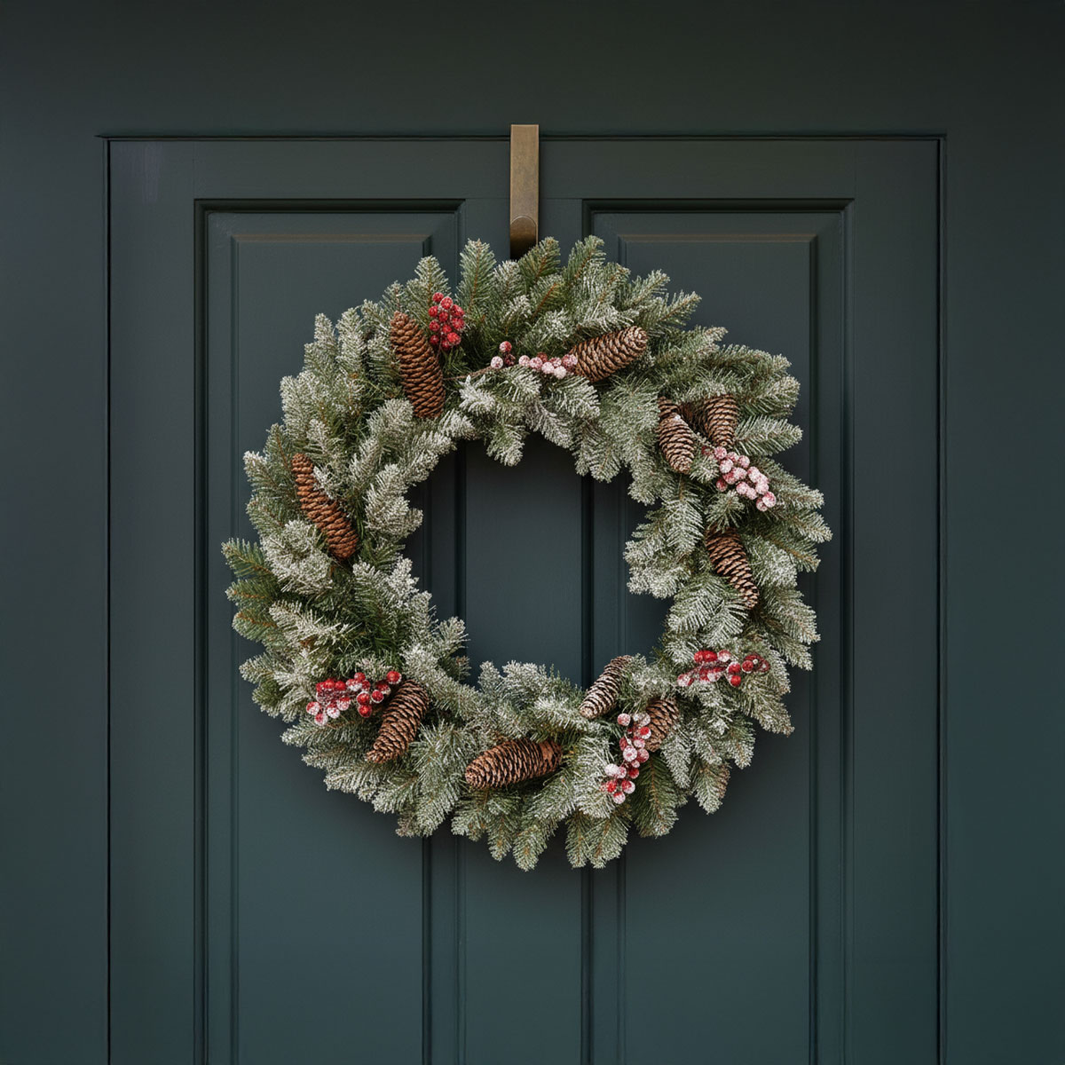 Couronne de Noël givrée avec des pommes de pin et des baies rouges sur une porte verte foncée