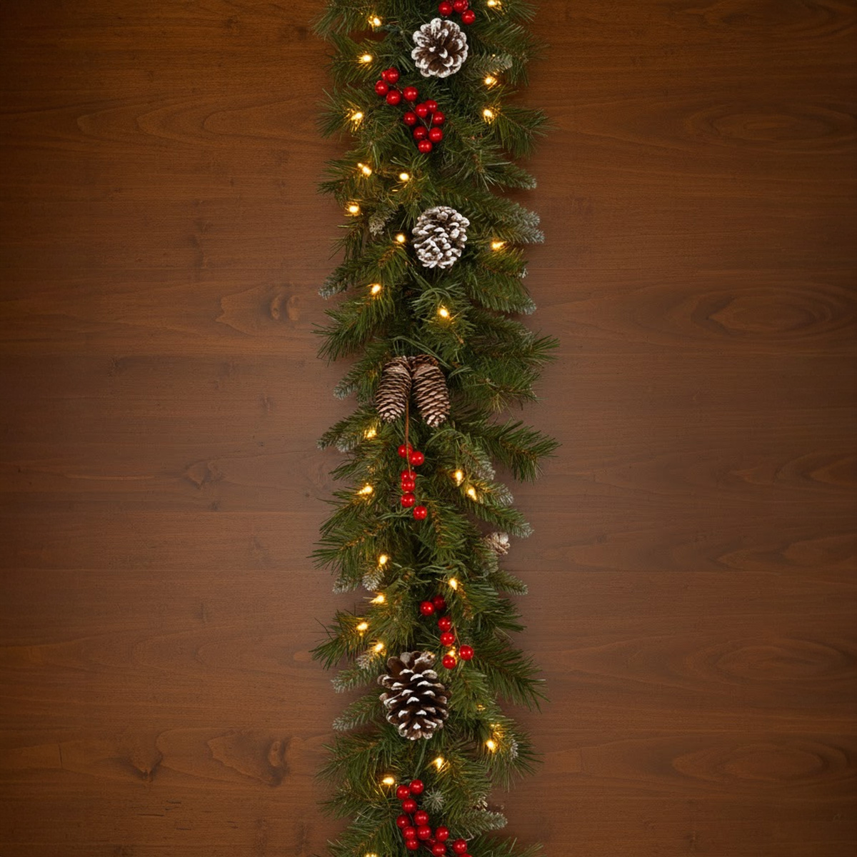 Christmas garland with pine cones, red berries and lights on a wooden background