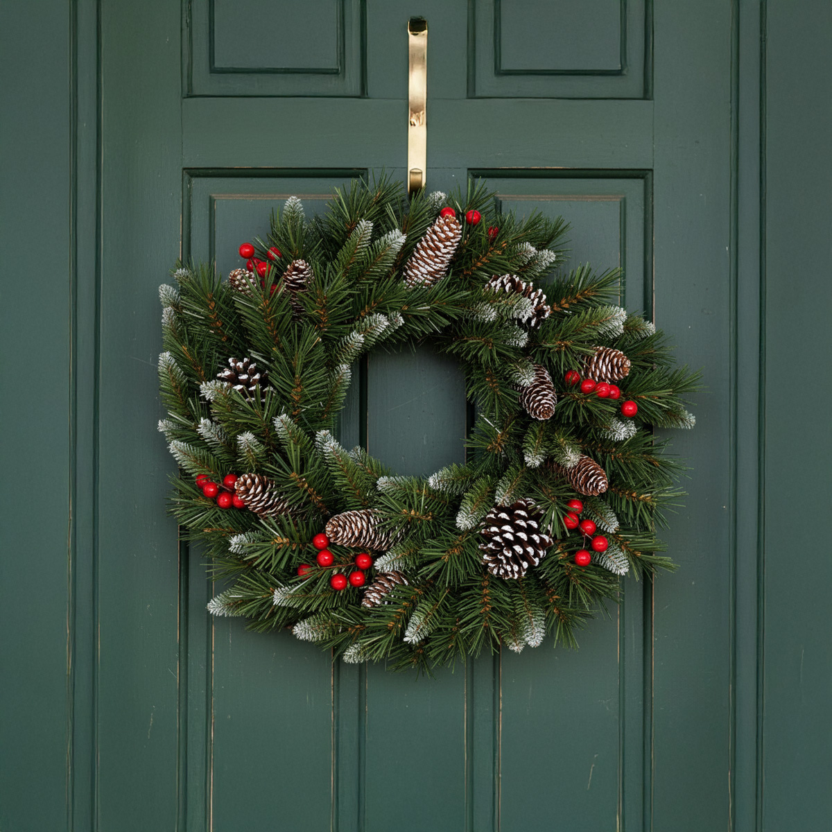 Couronne de Noël verte avec pommes de pin et baies rouges suspendue à une porte verte