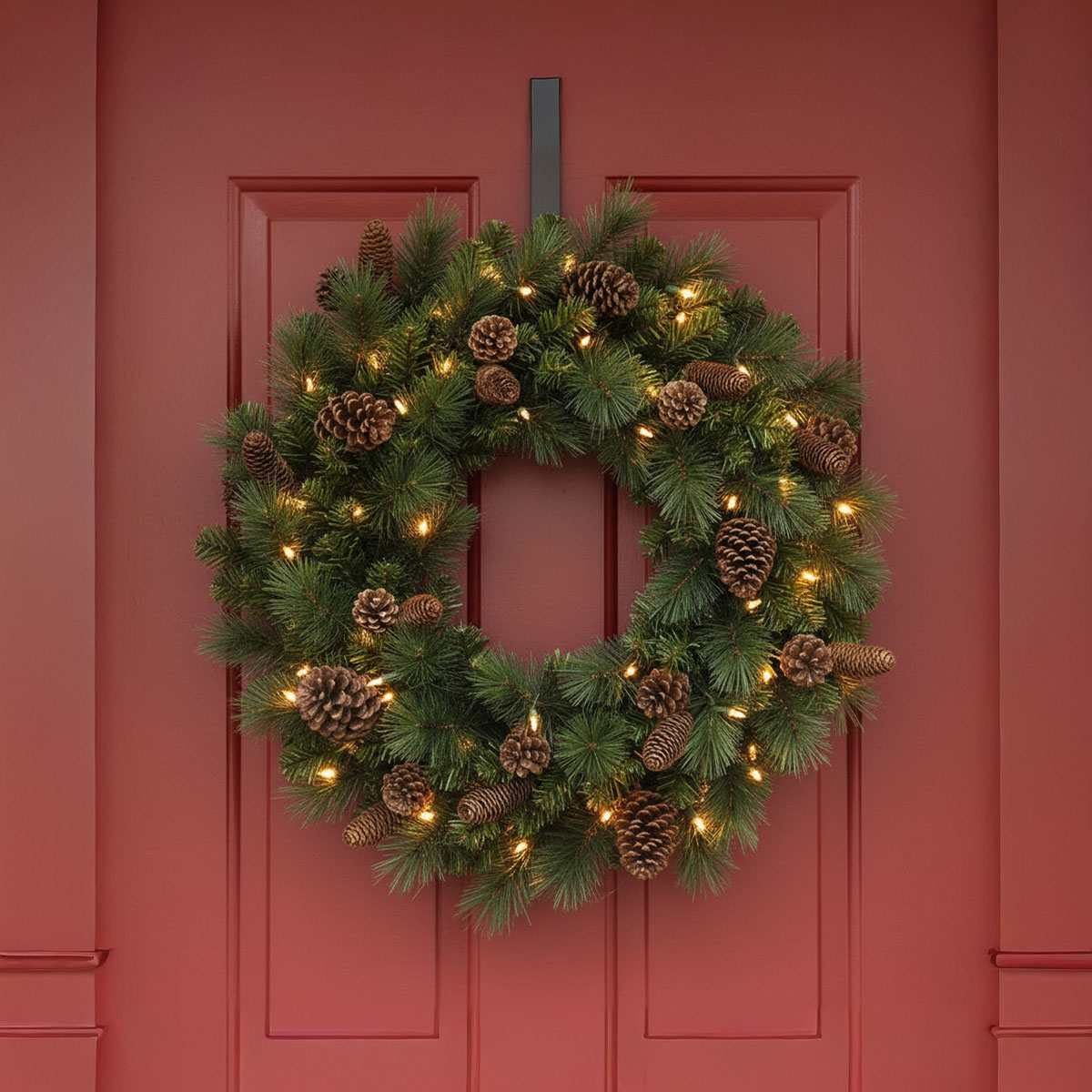 Couronne de Noël avec des pommes de pin et des lumières sur une porte rouge