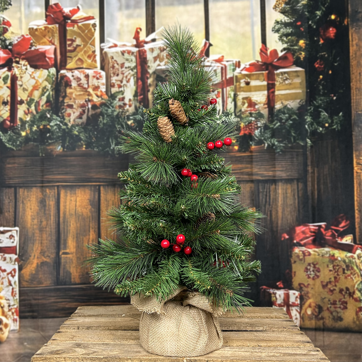 Petit sapin de Noël décoré de pommes de pin et de baies rouges, emballé dans un sac en toile de jute.