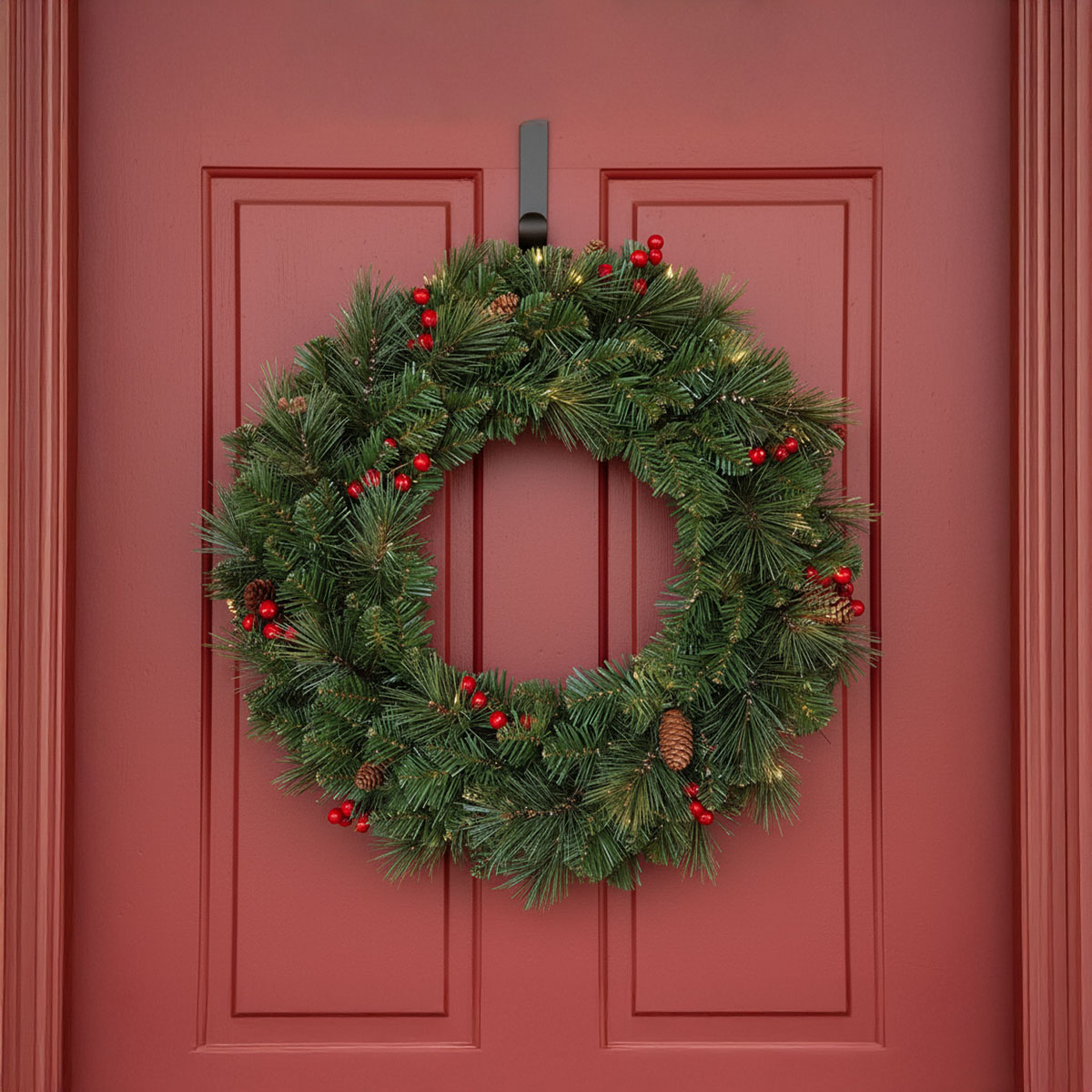 Couronne de Noël verte avec baies rouges et pommes de pin sur une porte rouge
