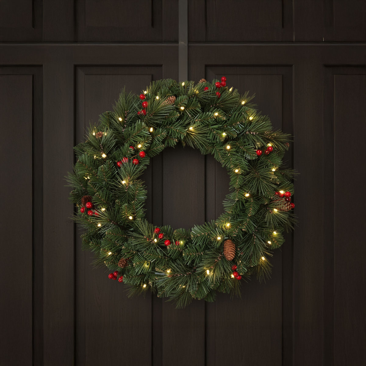 Couronne de Noël en pin avec baies rouges et lumières LED sur une porte sombre