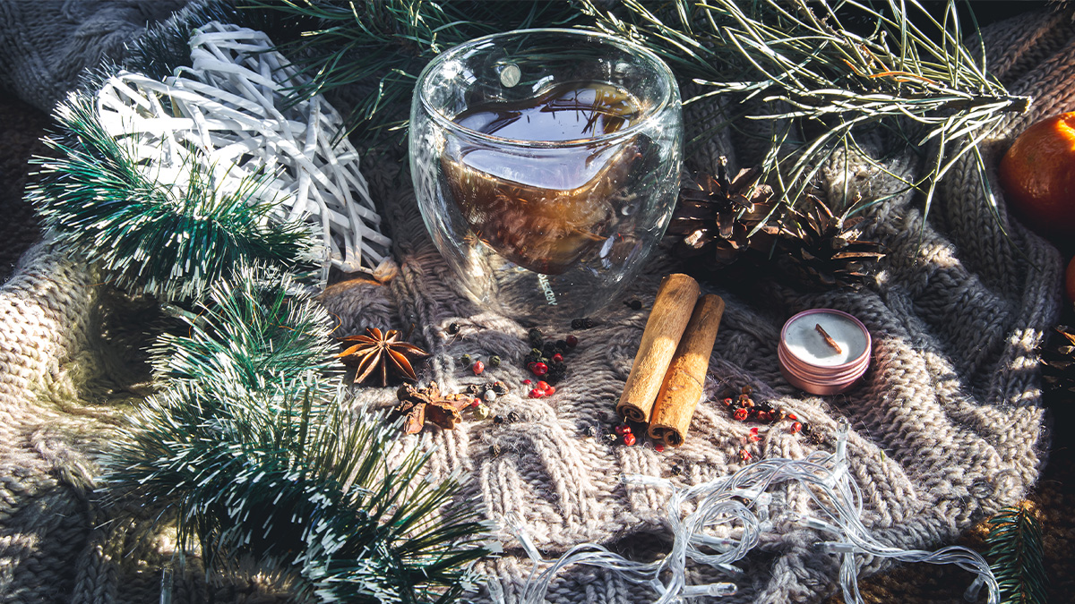 Boisson chaude d'hiver avec cannelle, épices, bougie, et décoration de Noël sur un pull en tricot.