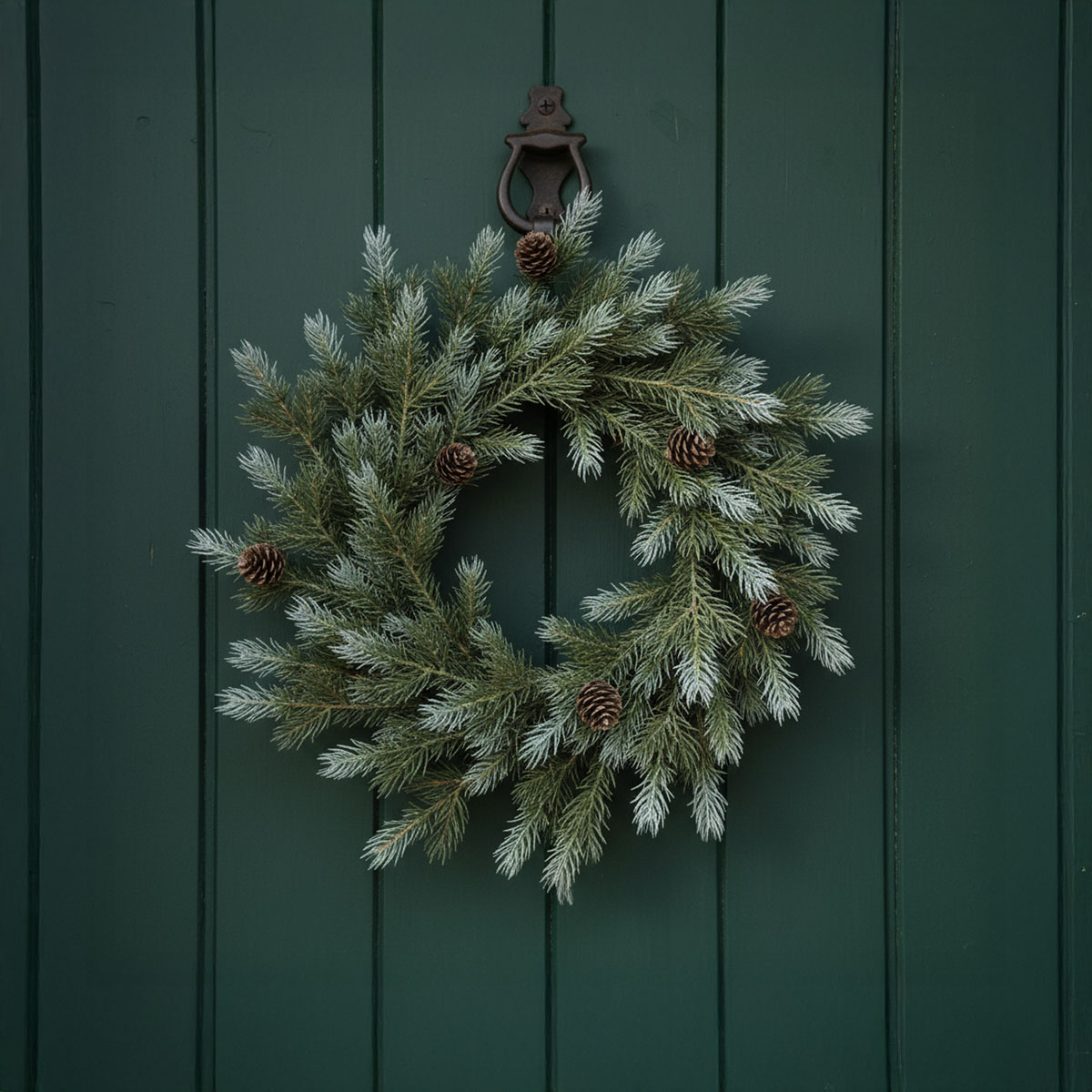 Couronne de sapin avec pommes de pin sur une porte verte