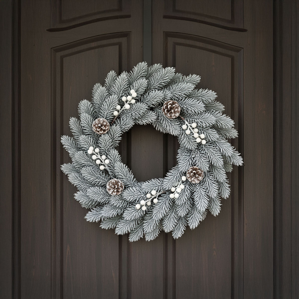 Couronne de sapin givrée avec pommes de pin et baies blanches sur une porte sombre