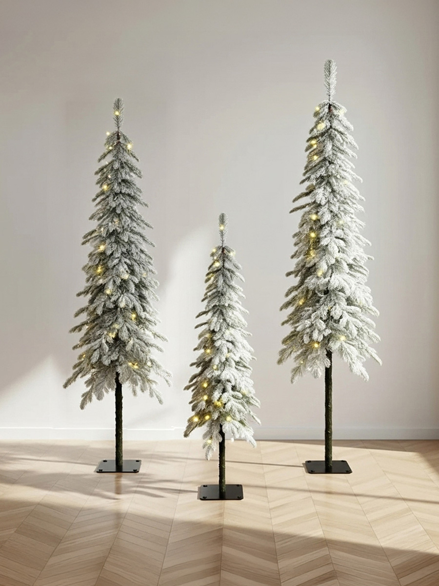 Trois sapins de Noël enneigés avec des lumières dorées sur un parquet