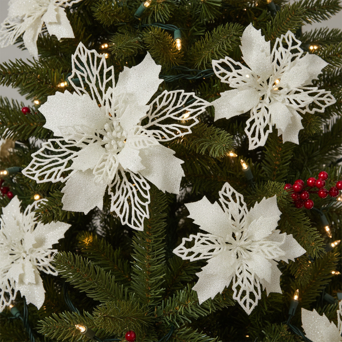 Fleurs de poinsettia blanches scintillantes sur un sapin de Noël décoré