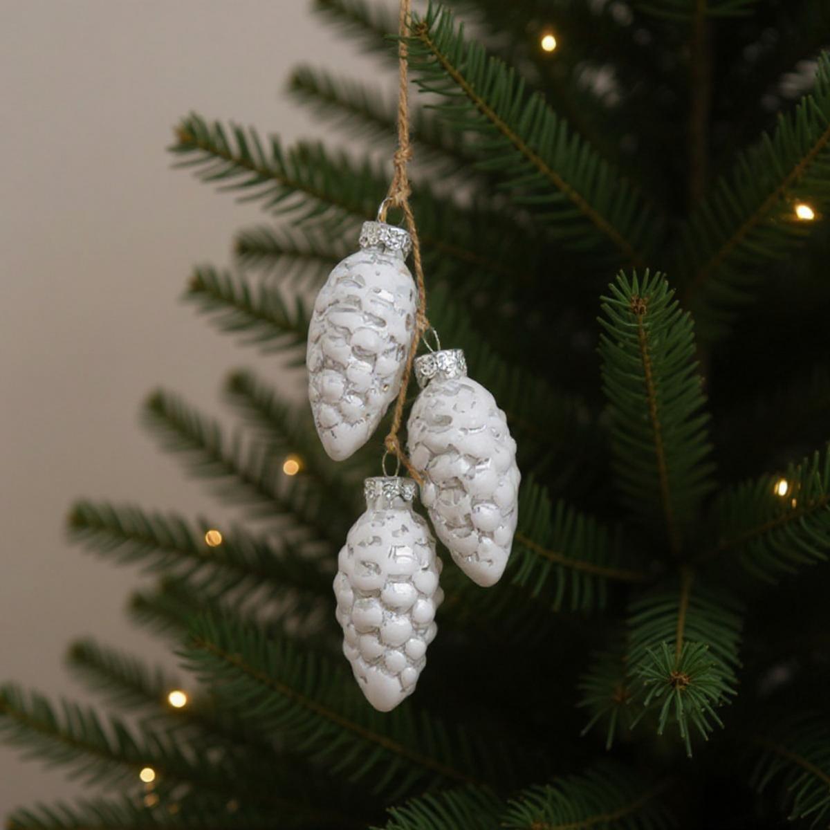Trois décorations de pommes de pin blanches suspendues à un sapin de Noël