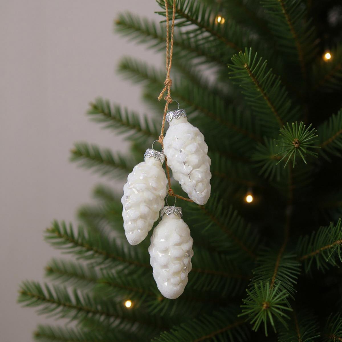 Trois décorations de pomme de pin blanches suspendues à un sapin de Noël