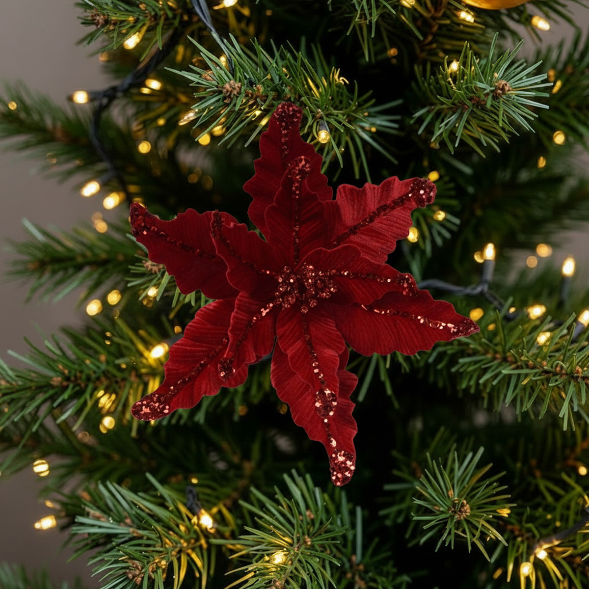 Fleur de Noël rouge pailletée sur un sapin décoré de guirlandes lumineuses