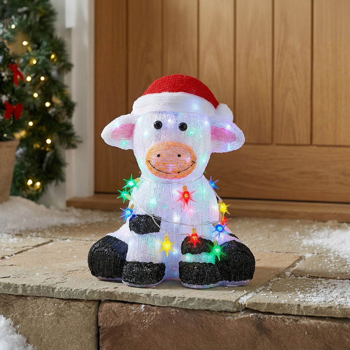 Vache de Noël lumineuse avec un bonnet de Père Noël et des guirlandes